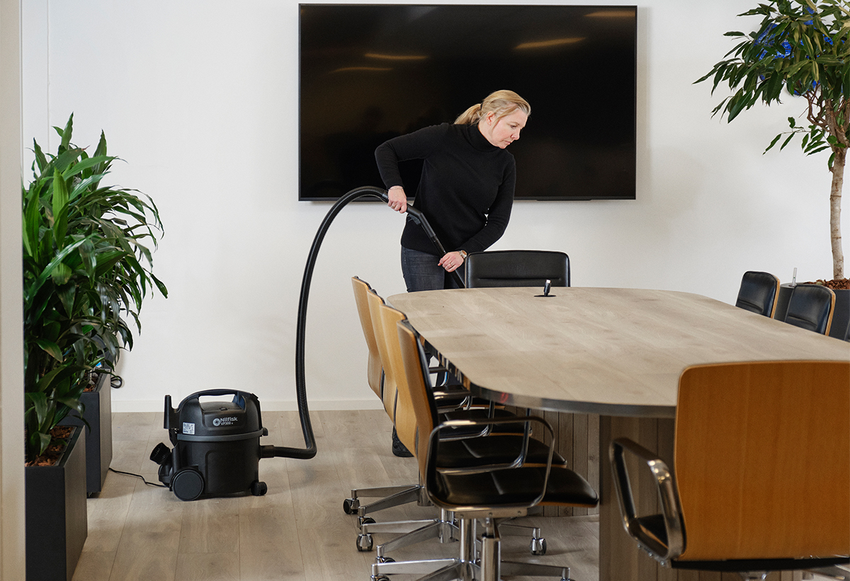 Απεικονξίζεται μια γυναίκα να καθαρίζει μια αίθουσα συναντήσεων.